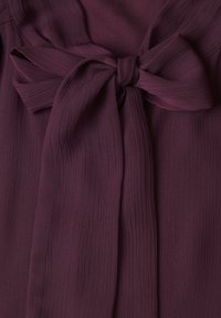 Tissu violet profond avec un motif texturé noué en un grand nœud décoratif au centre.