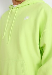 Neongrön Nike-hoodie i mjukt material med en känguruficka och snörning, samt en liten vit logotyp på bröstet.