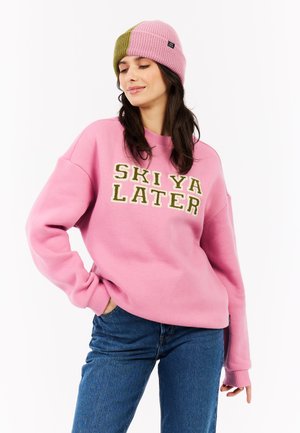 Roze sweatshirt met de tekst "SKI YA LATER" in het groen, gecombineerd met een twee-kleurige gebreide beanie in roze en groen. Casual pasvorm, zachte textuur.