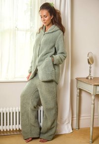 Zestaw odzieży dresowej z mikrofibry w miękkim zielonym kolorze, składający się z kurtki z kapturem z przednimi kieszeniami oraz spodni z szerokimi nogawkami. Przyjemna w dotyku tekstura, swobodny krój i bezszwowa konstrukcja.