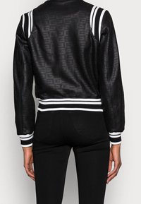 Veste bomber en cuir noir avec un dos à motifs, des accents à rayures blanches sur les épaules et les poignets, et un ourlet côtelé.