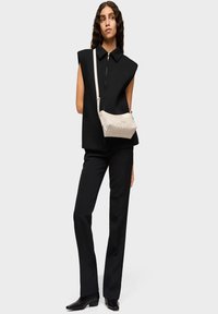 Top negro de gran tamaño sin mangas con cuello alto, combinado con pantalones negros ajustados. Se lleva un pequeño bolso beige claro con un patrón sutil de manera cruzada.