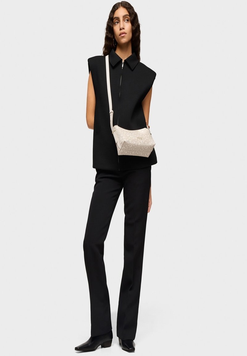 Top negro de gran tamaño sin mangas con cuello alto, combinado con pantalones negros ajustados. Se lleva un pequeño bolso beige claro con un patrón sutil de manera cruzada.