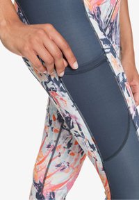 Legginsy z kolorowym, abstractowym wzorem w odcieniach niebieskiego, różowego i pomarańczowego. Gładki materiał z kontrastującymi ciemnymi panelami bocznymi i przeszyciami.