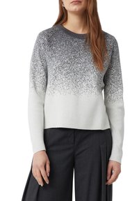 Jasnoszary sweter z gradientem srebrnego połysku na górze, okrągłym dekoltem i ściągaczami na rękawach, zestawiony z ciemnymi spodniami.