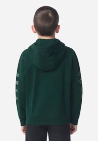 Sweatshirt verde escuro vista de costas, com capuz, punhos canelados e logótipos de crocodilo bordados ao longo da manga esquerda.