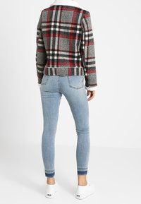 Rødt, sort og hvidt rutet jakkesæt i stof med en hvid faux fur-krave; parret med lyseblå skinny jeans og hvide sneakers.
