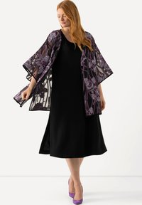 Un vestido negro combinado con un kimono transparente bordado en un diseño floral púrpura y lavanda. La modelo lleva tacones morados.