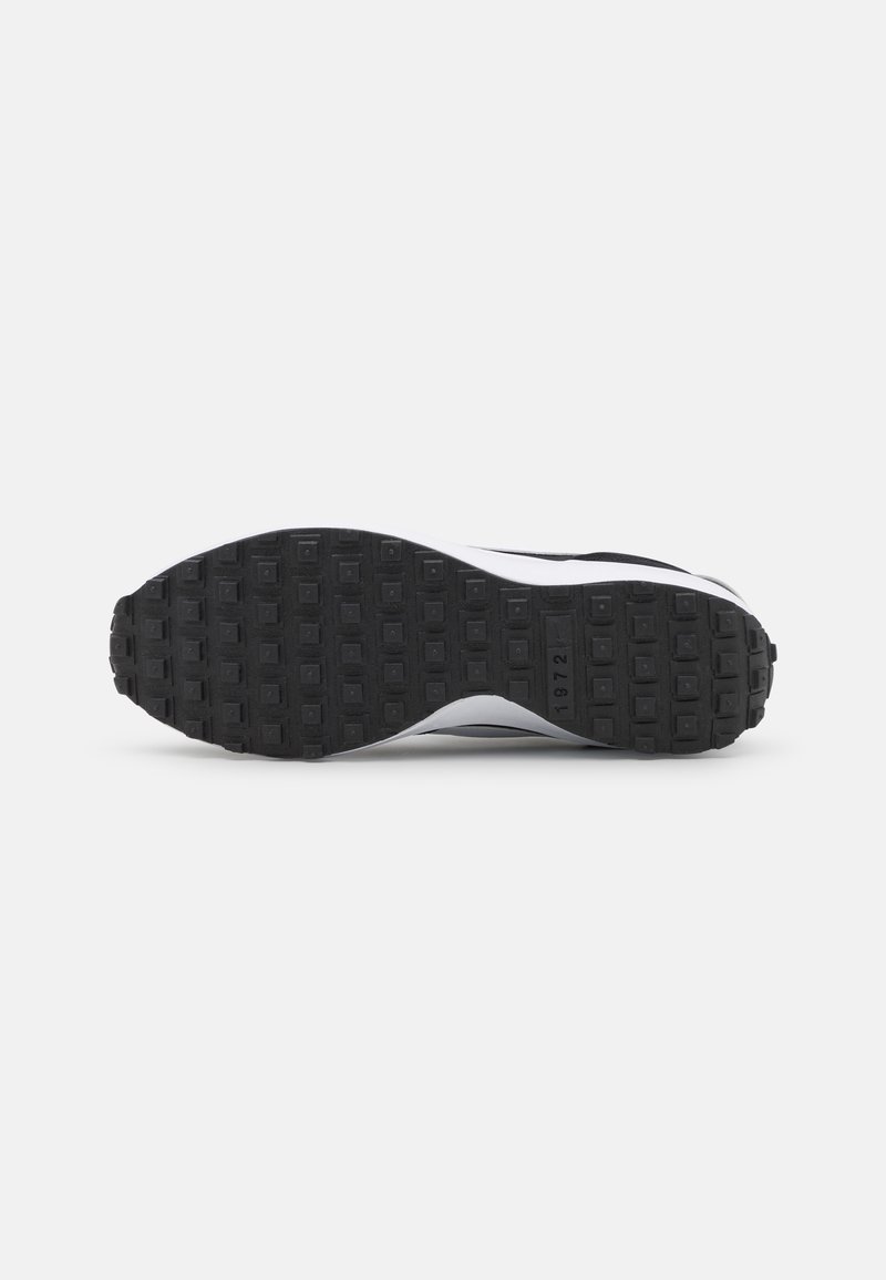 Suela de zapato atlético en blanco y negro que presenta una suela de goma texturizada con patrones cuadrados y una ligera curva hacia la zona del dedo del pie.