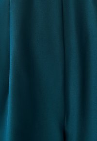 Grøntblåt stof med en glat tekstur, der har subtile diagonale vævemønstre og blød drapering, der fremhæver rene linjer og jævn farvefordeling.