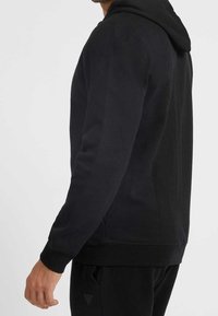 Felpa nera con cappuccio caratterizzata da una texture morbida, polsini aderenti e cappuccio con cordino, dal design slim e senza loghi o motivi visibili.