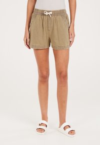 Pantaloni corti khaki con cordoncino e cintura elastica, dotati di tasche laterali e un tessuto a trama. Abbinati a sandali bianchi.