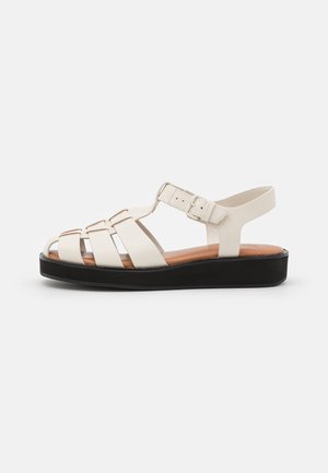 Białe skórzane sandały z wieloma paskami z przodu, zapięciem na sprzączkę i niską czarną podeszwą na platformie. Gładka faktura i otwarty nosek.