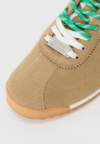 Brune suedesneakers med gummisåle, hvite og grønne lissser, og en metalllisselapp gravert med "Steve Madden."