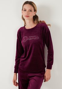 Burgundy long-sleeve top made of soft velvet with a round neckline, featuring embroidered text "follow your Dreams" and star accents.