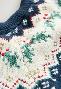 Sweter dziany z granatowym kołnierzem; kremowy korpus z zielonymi ostrokrzewami, czerwonymi jagodami oraz wzorzystymi pasami w odcieniach niebieskiego, zielonego i czerwonego.