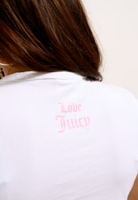Balta medvilnės marškinėliai su šviesiai rožiniu užrašu „Love Juicy“ ant nugaros. Audinys glotnus, su prigludusia forma.