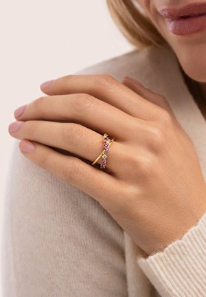 Anillo de tono dorado con diseño retorcido adornado con piedras preciosas multicolores. Acabado liso y banda delicada que realzan su apariencia elegante.