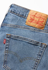 Blå denimjeans med en brun lærlap med teksten "Levi Strauss & Co." i midjen, med oransje søm og en liten rød etikett.