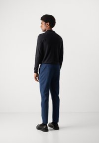 Zwarte langemouwen shirt, blauwe gestructureerde broek en zwarte schoenen. Het shirt heeft een aansluitend ontwerp en de broek heeft een elastische tailleband.