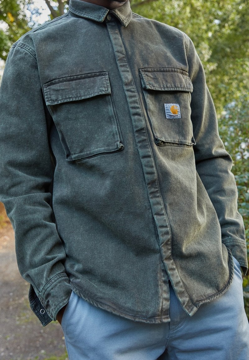 Oliwkowa, dżinsowa koszula z długim rękawem, z dwiema kieszeniami na piersi i żó�łtą naszywką z logo. Posiada kołnierzyk zapinany na guziki oraz zaokrąglony dół.