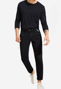 Chemise noire à manches longues avec un col rond, associée à un pantalon noir slim et des baskets blanches. Tissu lisse et doux avec un design minimaliste.