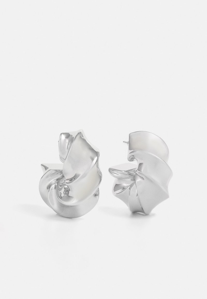 Sudeļi ar plūstošu spirālveida dizainu. Gluda tekstūra ar pulētu apdari. Iezīmējas ar maigu spīdumu un nav redzamu rotājumu.