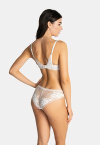 Soutien-gorge en dentelle blanche et culotte assortie, présentant des motifs floraux complexes et un filet semi-transparent, avec des bretelles ajustables et un détail en forme de nœud.