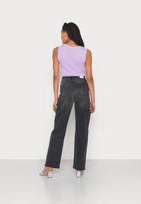 Top lilás sem mangas combinado com calças de ganga pretas de cintura alta. Sapatos são de um lilás claro, com salto bloco. Detalhes de costura visíveis nas calças.