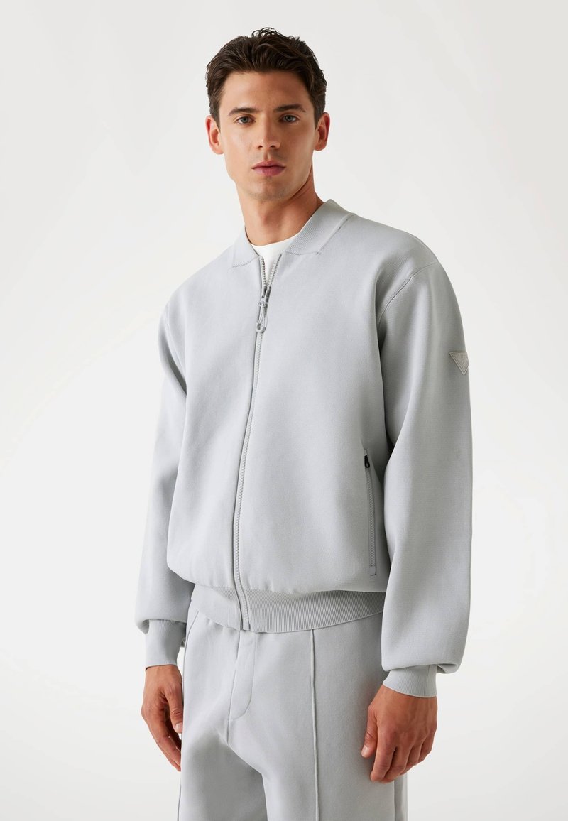 Light gray bomber jacket with a zip front, ribbed cuffs, and hem. Features side pockets and a textured finish.