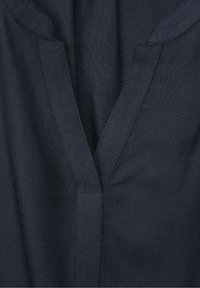 Navy blue kangas na muonekano wa texture, yenye muundo wa V na maelezo madogo ya kushona kando ya shingo na placket.