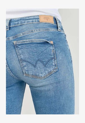 Blaue Denim-Jeans mit einer leicht ausgebleichten Textur, die eine Gesäßtasche mit einem charakteristischen, geschwungenen Stichmuster sowie einem Leder-Logo-Patch aufweist.