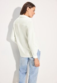 Hellgrünes Langarmhemd mit Kragen, im lässigen Schnitt und mit subtiler Textur, kombiniert mit hellblauen, lässig geschnittenen Jeans.