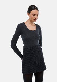 Haut ajusté à manches longues gris foncé associé à une mini-jupe à carreaux texturée avec deux poches avant et une taille lisse.