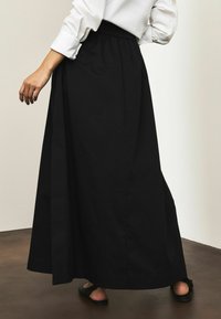 Falda larga negra de tela suave, con cintura elástica y corte holgado, presenta una abertura lateral y un largo hasta el tobillo.