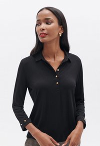 Polo shirt nero a maniche lunghe in tessuto morbido, con bottoni dorati e collo a battente, polsini con bottone e vestibilità slim.