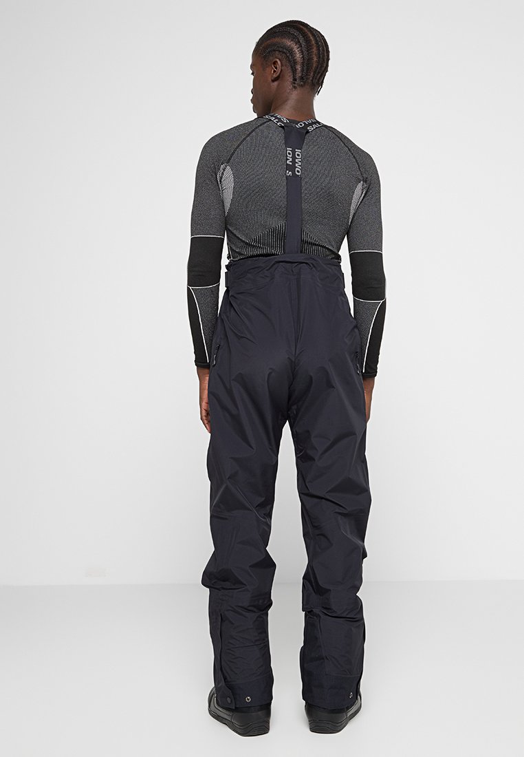 Zwarte waterdichte skibroek met verstelbare banden en een ritszak, gecombineerd met een aansluitend grijs longsleeve shirt met textuuraccenten.