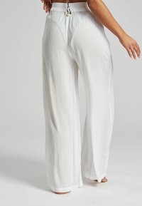 Pantalones de pierna ancha blancos, confeccionados con una tela texturizada, que presentan una cinturilla elástica fruncida y un detalle de cordón en la parte trasera.