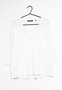 Valkoinen, löysästi istuva, pitkähihainen paita V-pääntielle. Valmistettu kevyestä kankaasta, jossa on suora helma ja hieman pidempi takaosa.