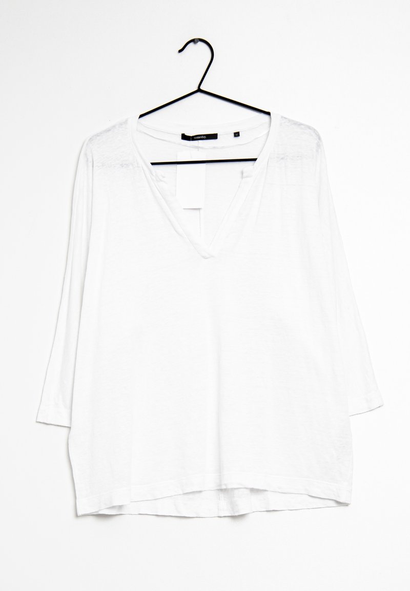 Biała, luźna bluzka z długim rękawem i dekoltem w kształcie litery V. Wykonana z lekkiego materiału, ma prosty dół i lekko wydłużony tył.