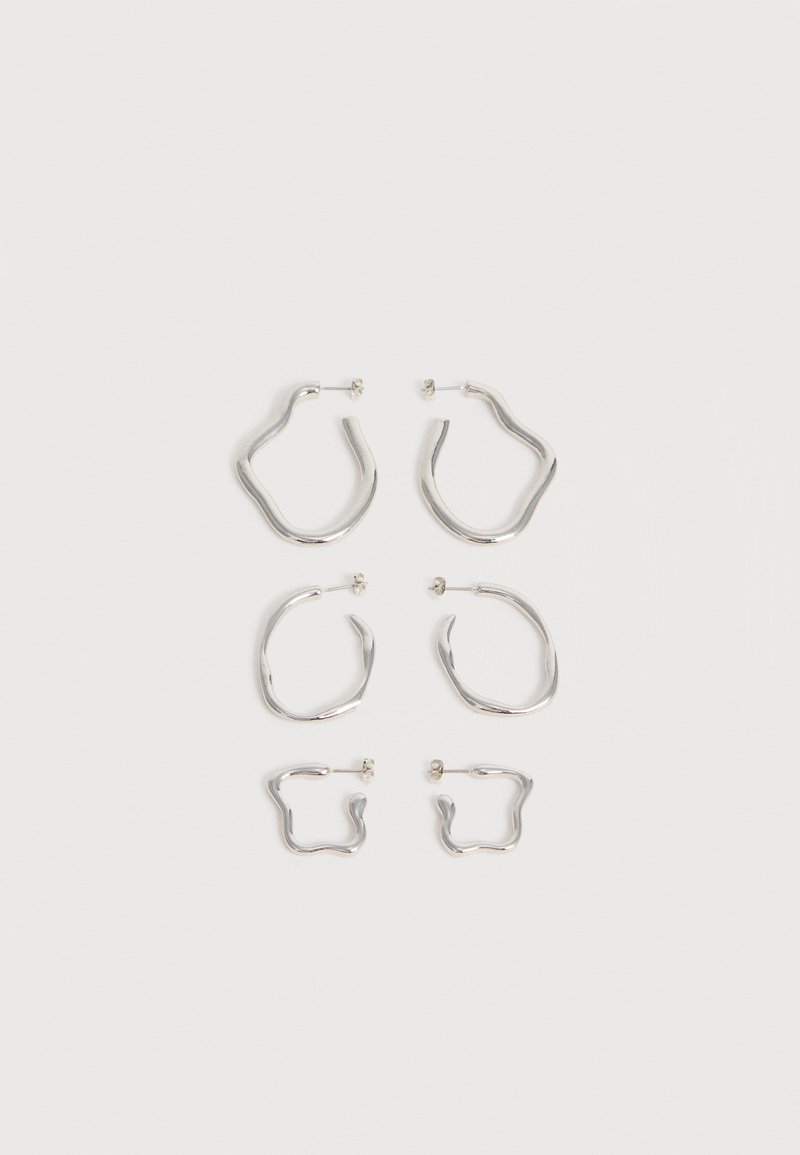 Τρία ζευγάρια ασημένια σκουλαρίκια σε ακανόνιστο σχήμα, σε μεγάλες, μεσαίες και μικρές διαστάσεις, τοποθετημένα κάθετα σε λευκό φόντο.