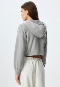 Sudadera gris recortada con un acabado texturizado, mangas largas, capucha y puños elásticos, combinada con pantalones de chándal crema de cintura alta.