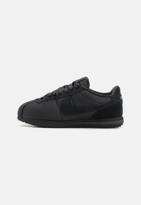 Černá sportovní bota s textilním a semišovým svrškem, texturovanými tkaničkami, kulatou špičkou a vroubkovanou gumovou podrážkou. Obsahuje černé logo na boku.