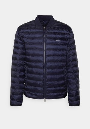 Navy puffer jacket with a lightweight, quilted design, ribbed collar, and front zipper. Features a subtle logo on the chest.