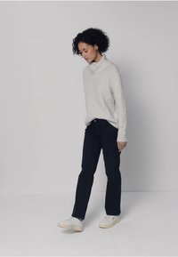 Ljusgrå grovstickad tröja med en polokrage, tillsammans med mörkblå jeans och vita sneakers, mot en enkel vit bakgrund.