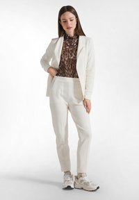 Witte textuur blazer en bijpassende broek over een bruin dierenprint top, gecombineerd met chunky witte sneakers.