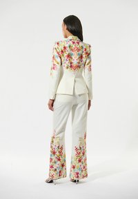 Completo floreale bianco con giacca aderente caratterizzata da vivaci motivi floreali rosa, blu e verdi. I pantaloni a campana completano il design.
