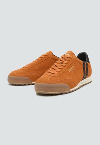 Pomarańczowe zamszowe sneakersy z czarnymi paskami, gumowymi podeszwami i wyściełaną cholewką. Posiadają okrągły czubek i teksturowaną powierzchnię dla lepszej przyczepności.