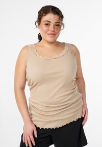 Beige geripptes Tanktop mit Spitzenbesatz am Ausschnitt und gerafftem Saum. Das Design ist figurnah geschnitten mit einer glatten, weichen Textur, getragen zu dunklen Shorts.
