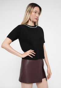 Black short-sleeve sweater with a round neckline adorned with decorative beads, paired with a dark burgundy leather mini skirt.